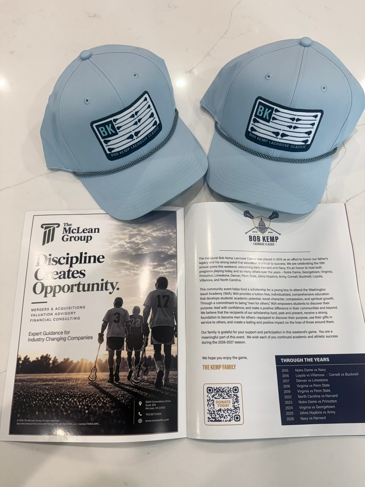The McLean Group ad in the Bob Kemp Lacrosse Classic program beside two event caps